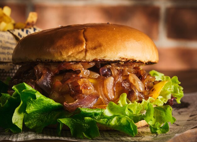 Burger au boeuf et oignons caramélisés sur une planche de bois. Cheeseburger à l'oignon et au bœuf. Délicieux burger fait maison juteux.