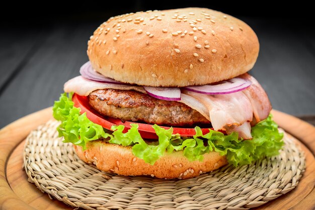 Burger de bacon avec escalope de boeuf, avec des légumes frais, sur fond de bois