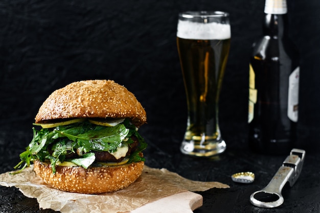 Burger et bière dans un verre sur fond sombre. Hamburger