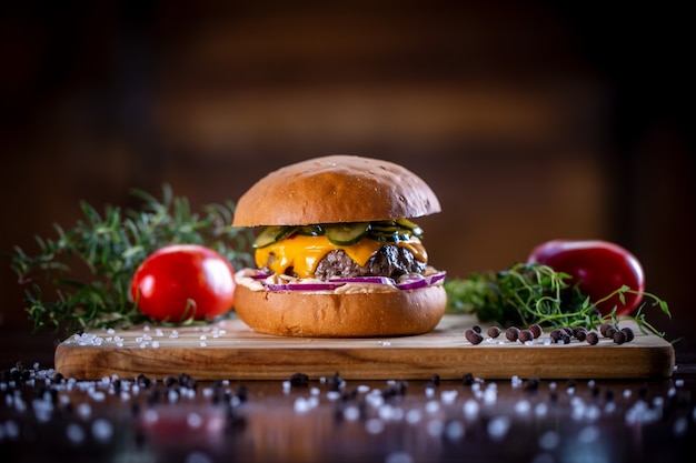 Burger de boeuf artisanal avec cheddar, bacon, cornichons, oignon violet et sauce sur fond de bois