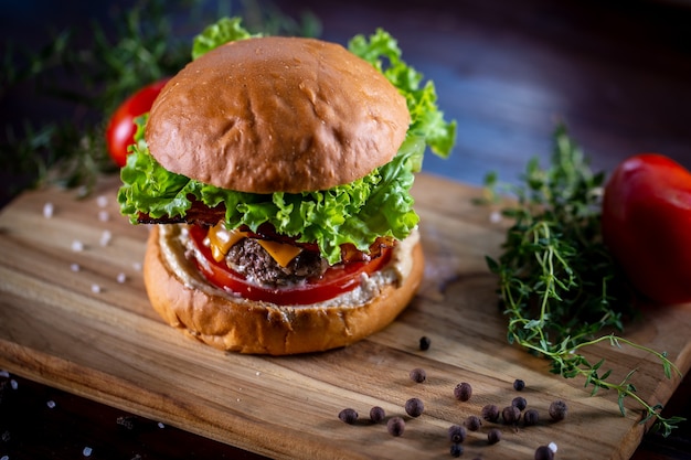 Burger de boeuf artisanal avec cheddar, bacon, laitue et sauce sur fond de bois