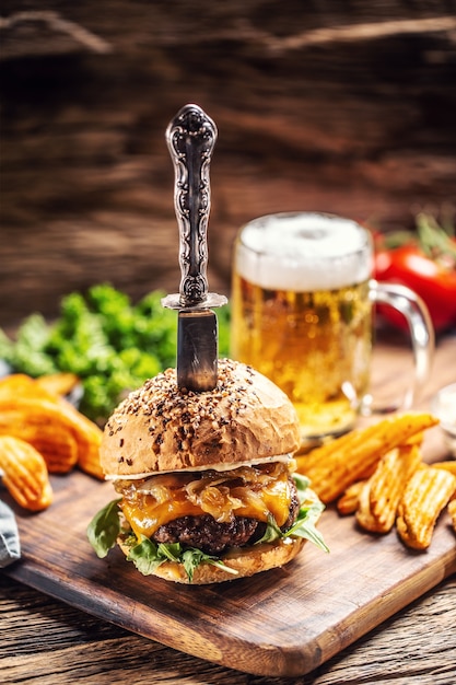 Burger de boeuf aux oignons caramélisés et roquette dans un environnement rustique en bois, une bière et des quartiers de pommes de terre en accompagnement.