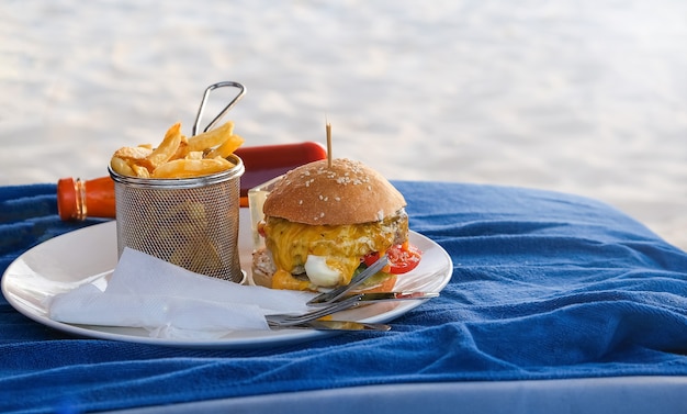 Burger de boeuf classique avec fromage et frites. sur plaque blanche. Restauration rapide sur la plage. Mise au point sélective.