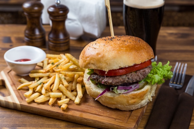 Burger chaud servant sur une planche de bois avec de la bière brune