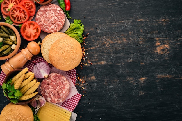 Burger cru Cuisiner un hamburger avec de la viande Sur un fond en bois noir Vue de dessus Espace de copie gratuit