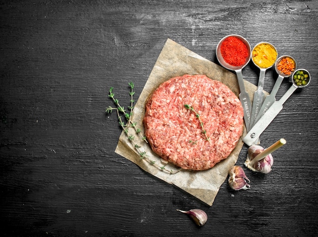 Burger cru avec des épices et des herbes sur le tableau noir