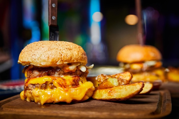 Photo burger avec deux galettes de bœuf un pain et du fromage avec un couteau coincé dedans servi avec des pommes de terre au four