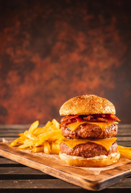 Burger double boeuf et bacon avec fromage cheddar et frites sur une planche en bois