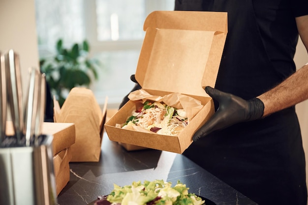 Photo burger frais avec des légumes l'homme emballe de la nourriture dans des boîtes de papier écologiques restaurant intérieur