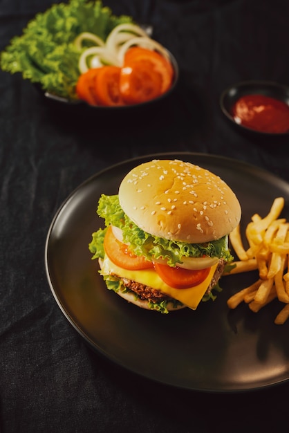 Burger frais et savoureux sur une planche à découper avec des frites, du ketchup et du cola en verre sur fond noir