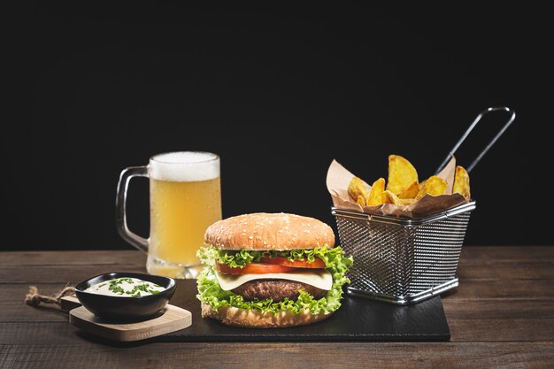 Burger avec frites et bière sur base en bois sur fond noir