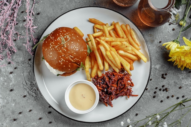 Photo burger avec frites et sauce sur une plaque blanche