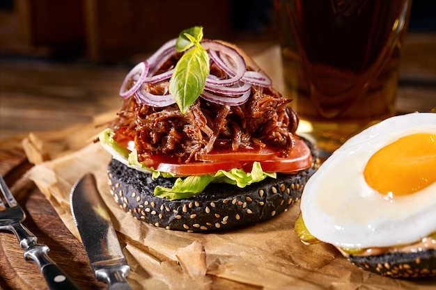 Burger juteux sur la planche, fond noir. Fond sombre, restauration rapide. Cuisine américaine traditionnelle. Espace de copie.