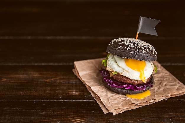 Burger noir délicieux et juteux avec une grande côtelette de viande sur fond noir