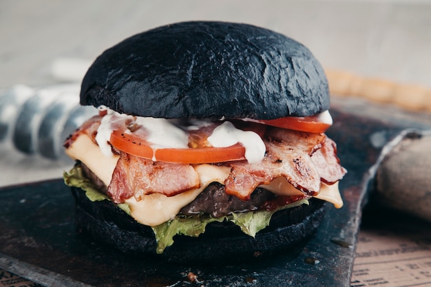 Burger noir avec de la viande sur une planche ronde en bois avec une hache