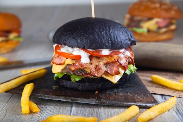 Burger noir avec de la viande sur une planche ronde en bois avec une hache