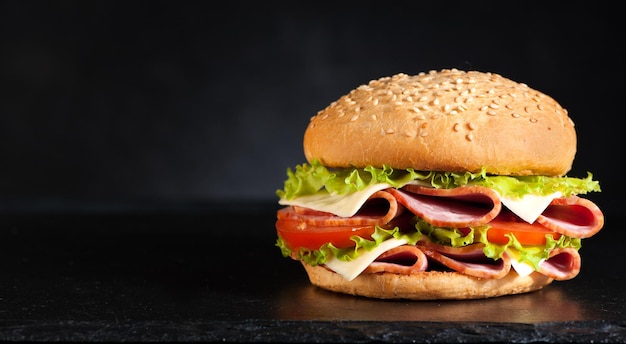 Burger sandwich au jambon fromage et légumes sur fond noir et espace pour le texte