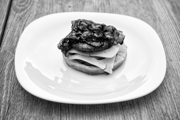 Burger sandwich avec pain bun boeuf rencontrer des tranches de fromage et du ketchup de tomate sur une plaque blanche sur fond en bois Restauration rapide manger concept de régime alimentaire malsain