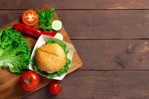 Burger, tomate, concombre, laitue, poivre sur une table en bois sombre