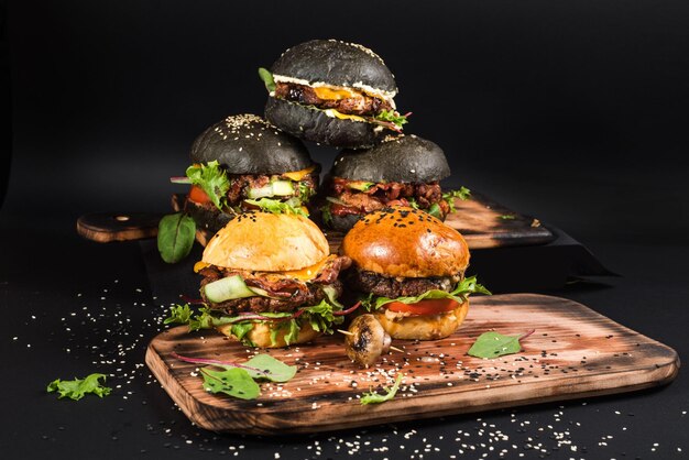 Burgers artisanaux assortis avec différentes garnitures, avec des graines de sésame sur fond noir