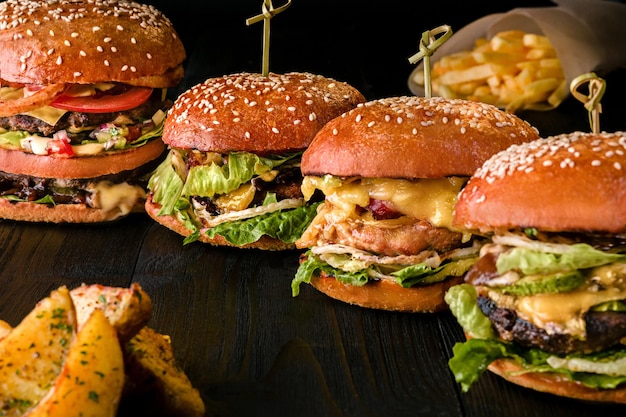 Photo burgers assortis avec différentes garnitures, avec des graines de sésame sur une table en bois isolée sur fond noir. carte du bar