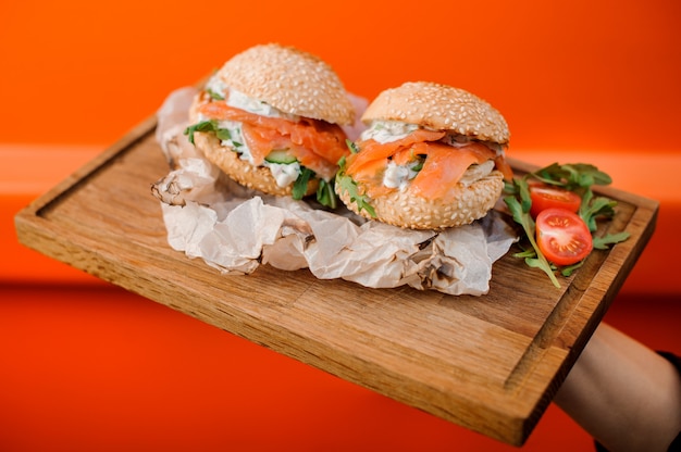 Burgers froids au saumon, sauce, concombre, tomate et roquette servis dans l'assiette en bois