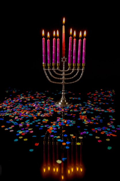 Burning menorah avec des bougies roses et des confettis sur fond noir. Symbole de la fête juive de Hanoukka.