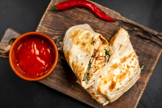 Burrito s'enroule avec du poulet et des légumes sur une planche à découper, sur un fond de béton, shawarma mexicain