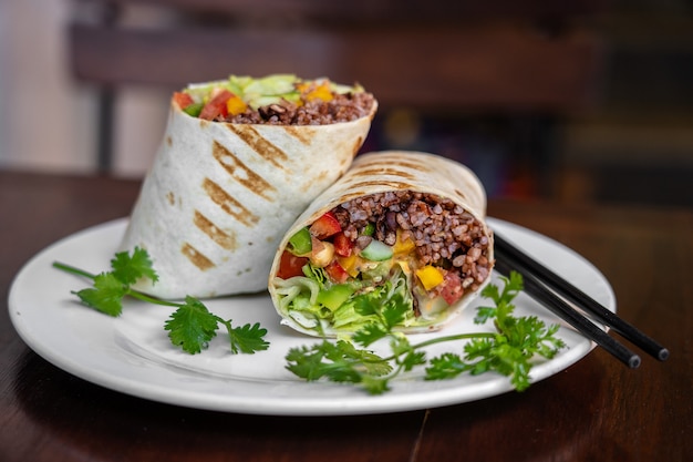 Burrito végétalien. Enveloppement d'aliments crus tranchés avec des ingrédients végétaliens sur une assiette. Fermer