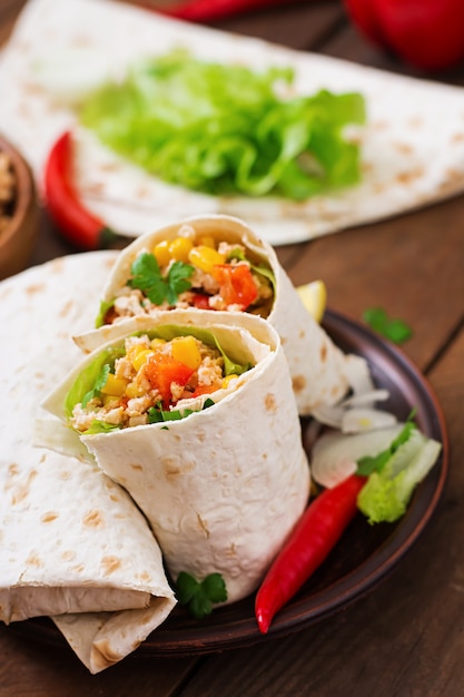 Burritos s'enroule avec de la viande de poulet, du maïs, des tomates et des poivrons sur une table en bois