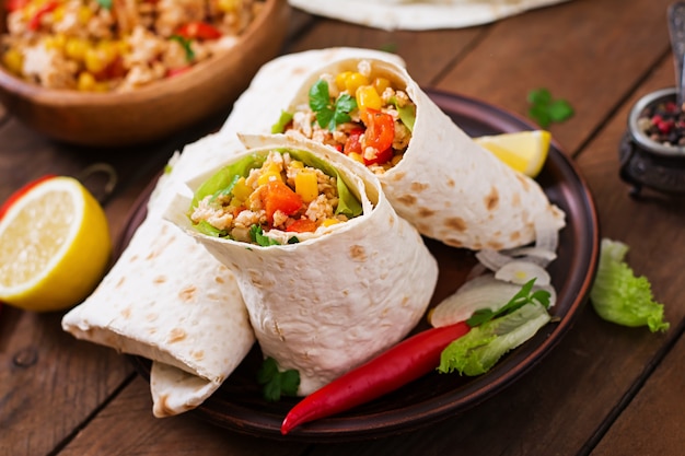 Burritos s'enroule avec de la viande de poulet, du maïs, des tomates et des poivrons sur une table en bois