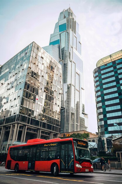 un bus rouge roule sous des gratte-ciel en verre