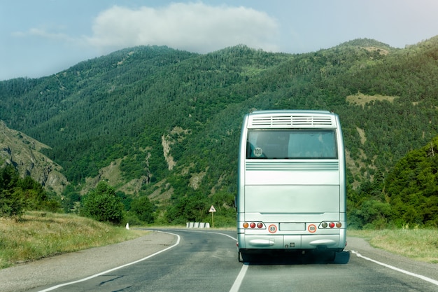 Photo bus touristique sur la route entre les montagnes verdoyantes. vue arrière