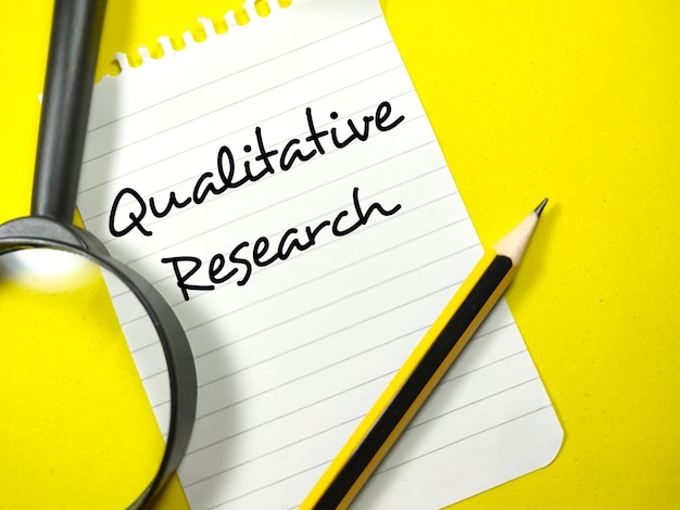 Business conceptText Recherche qualitative écrit sur papier à lettres avec un crayon et une loupe sur fond jaune