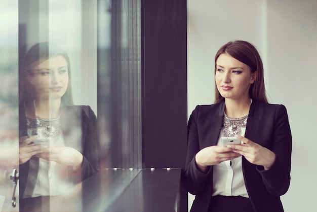 Business Girl debout dans un bâtiment moderne près de la fenêtre avec téléphone