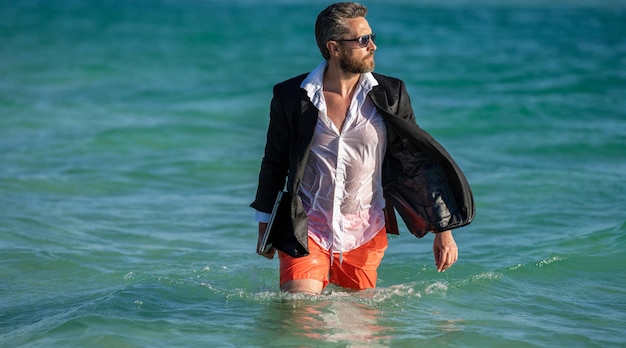 Businessman chef costume se détendre sur la plage homme d'affaires avec ordinateur portable en tenue formelle près de la plage tropicale chaude affaires été patron d'affaires passer le week-end à la plage voyage et détente