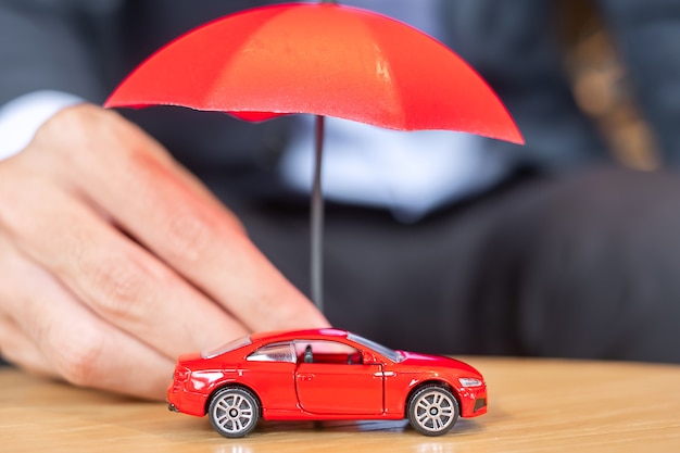 Businessman hand holding parapluie couverture ou protection jouet de voiture rouge sur table