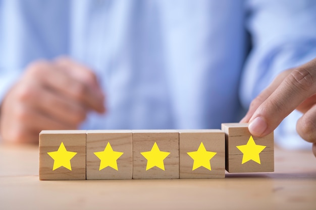 Businessman hand putting yellow star qui est imprimé sur un cube en bois. Enquête d'évaluation client et concept de satisfaction.