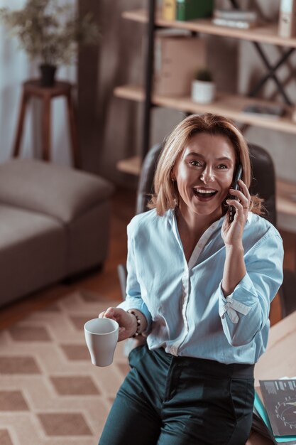 Buvant du café. Femme mature aux cheveux blonds buvant du café et appelant son mari