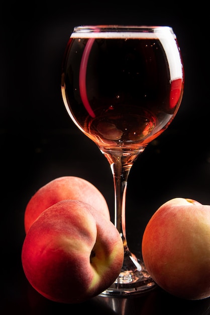 Buvez un verre de vin mousseux avec des pêches autour et une mise au point sélective sur fond noir