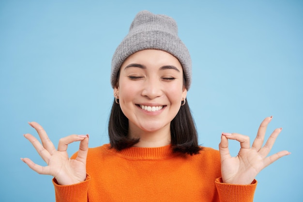 Ça sonne l'esprit dans un corps sain souriant fille asiatique calme et détendue en beanie montre gestu de relaxation zen