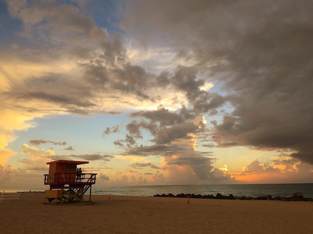 Cabane de sauveteur sur la plage contre un ciel nuageux au coucher du soleil