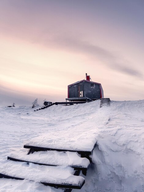 Cabanes en hiver. Escalier couvert de neige menant à travers les congères à une maison isolée sur une colline le soir. Vue verticale.