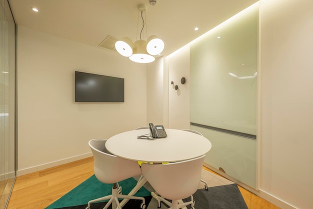 Cabine de bureau avec table ronde chaises pivotantes blanches tv sur le mur et porte coulissante en verre