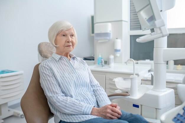 Cabinet dentaire. Femme aînée s'asseyant au bureau de dentistes et attendant le docteur