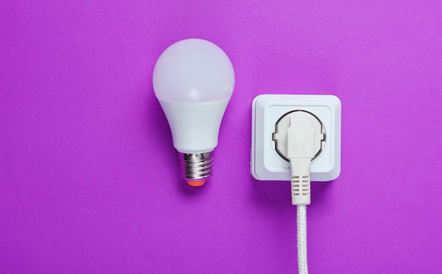 Câble blanc branché sur la prise de courant et ampoule LED sur table violette. Vue de dessus