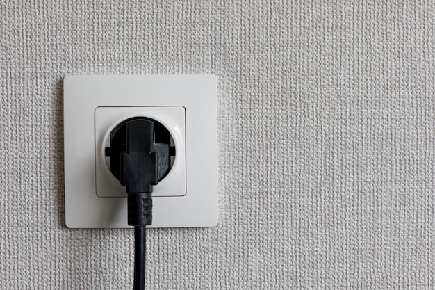 Photo un câble électrique noir branché sur une prise murale européenne sur un mur en plâtre blanc avec un espace de copie