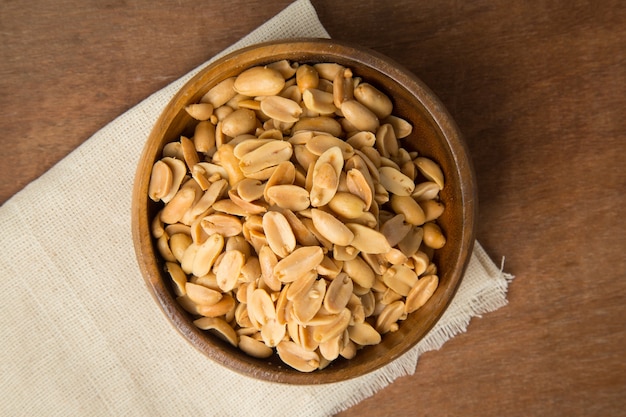 Cacahuètes grillées dans un bol en bois mettant sur lin et fond en bois.