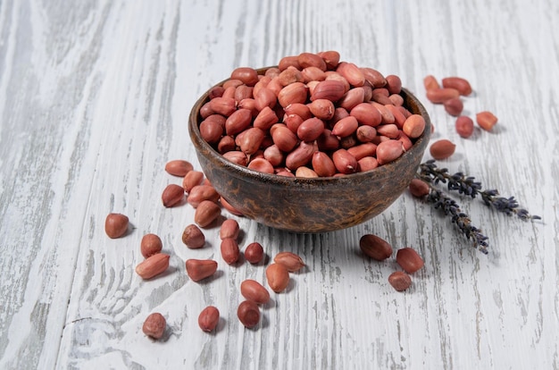 Les cacahuètes sont crues rouges dans une tasse en bois sur un fond en bois blanc Style rustique Le concept de collations végétariennes et diététiques