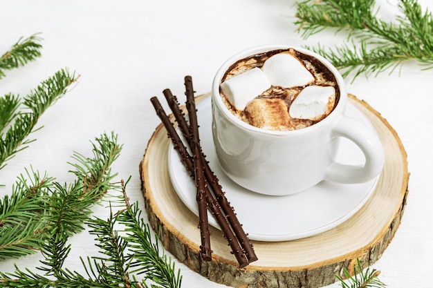 Cacao chaud avec guimauves décoré de branches de pin sur bois blanc